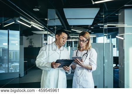 Two Doctors, Mixed Race Asian Man And Caucasian Woman, Communicate, Discuss Patient Treatment, Work 