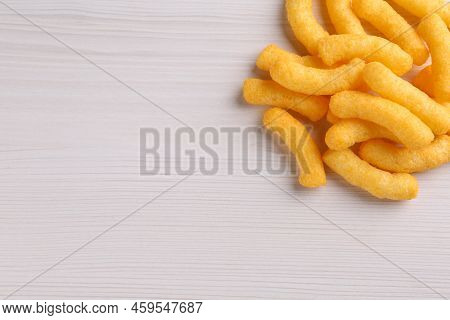 Heap Of Tasty Cheesy Corn Puffs On White Wooden Table, Flat Lay. Space For Text