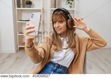 Joyful Young Blonde Lady In Warm Sweater In Headphones Listen Fav Songs Doing Selfie Video Call Sitt