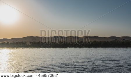 Serene Evening Landscape. The River Flows Calmly. The Sun Is Low Over The Sand Dunes. Green Vegetati