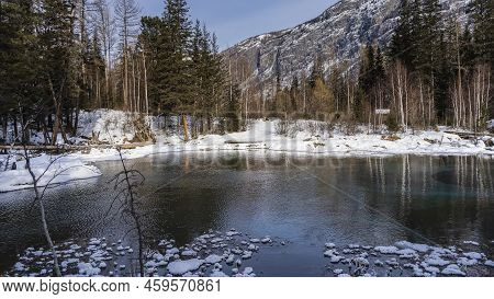 A Unique Ice-free Lake In The Winter Forest. Trees On Snow-covered Shores. Islands Of Frost On The S
