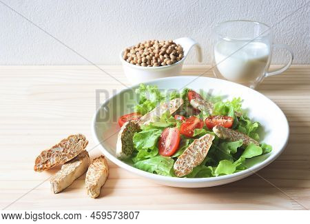 Front View Of  Tempeh In Salad Dish, Soy Bean Seeds In White Bowl, And Soy Milk On Wooden Table, Pro