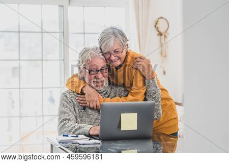 Couple Of Two Happy Seniors Working And Using Laptop Together At Home Smiling And Having Fun Togethe