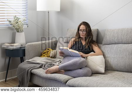 Brunette Woman With Long Hair Sitting On The Couch In The Appartment And Reading The Book