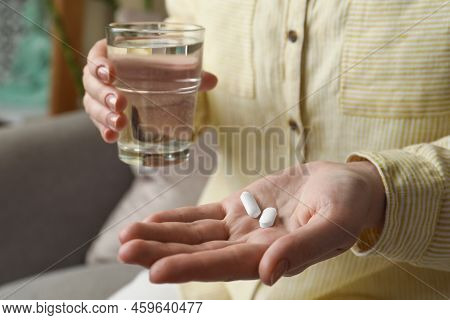 Calcium Supplement. Woman Holding Glass Of Water And Pills Indoors, Closeup