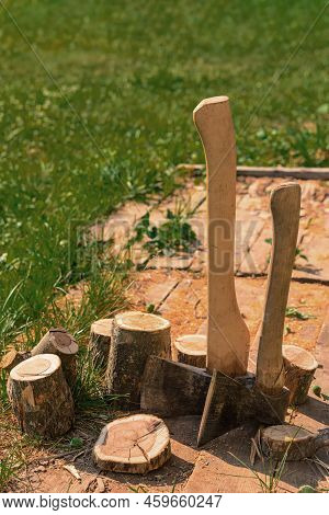 Axes Stand Next To Wooden Chocks. Preparation Of Firewood For Kindling. Stumps With Axes Illuminated