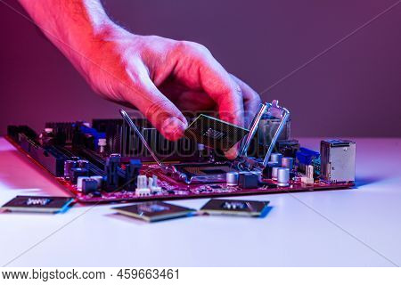 A Man's Hand Inserts A Processor Into The Motherboard Socket.