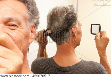 Mature Man 60plus Combing His Mostly Gray Hair In The Back Of His Head In Front Of A Mirror