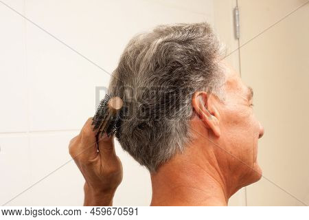 Mature Man 60plus Combing His Mostly Gray Hair In The Back Of His Head In Front Of A Mirror