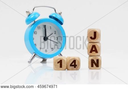 14st Of January. Wooden Cube Calendar For January 14, Next To A Blue Alarm Clock. Objects On A Refle