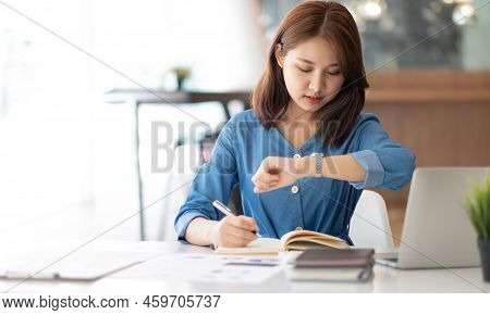 Smiling Pretty Girl Working On Laptop Computer While Sitting At Office Table, Taking Notes In A Diar