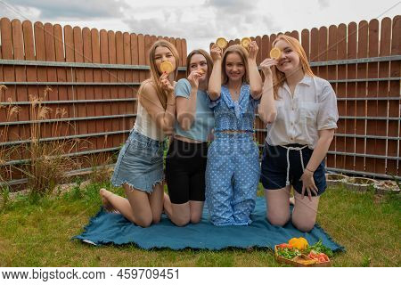 Portrait Of Young Joyful Beautiful Women Covering Eyes With Slices Of Orange, Standing On Knees On P
