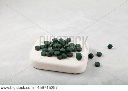 Pile Of Green Pills On White Wooden Podium. Selective Focus, Copy Space. Natural Chlorella And Spiru