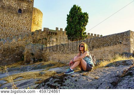 Mature Tourist Woman Sitting On A Stone Next To A Medieval Castle With Wall, Puente Congosto, Salama