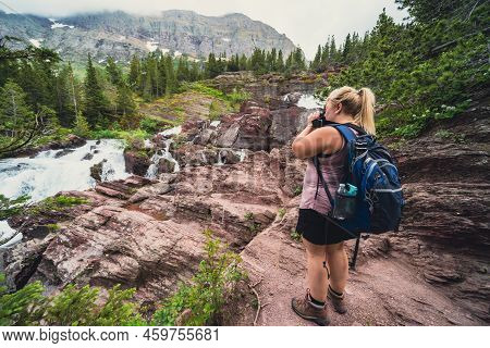 Blonde Hiker Woman Takes Photos At Redrock Falls Along Swiftcurrent Pass Hiking Trail In Glacier Nat
