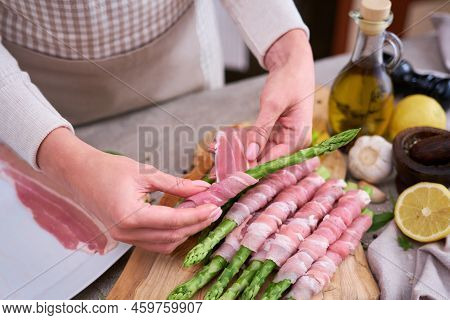 Woman Cooking Green Aspargus Covered With Bacon At Domestic Kitchen