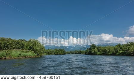 The Bed Of The Blue River Bends Between The Banks Overgrown With Lush Green Vegetation. A Mountain R