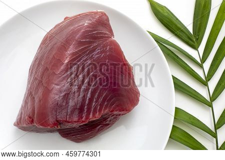 Piece Of Raw Tuna Fish Meat On White Plate With Green Palm Leaf On The Side. Top View Closeup.