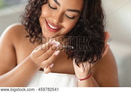 Split Ends Treatment. Black Chubby Lady Applying Serum On Damaged Dry Hair, Using Cosmetics For Hair