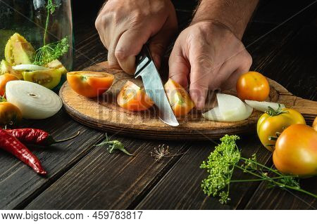 Cooking Adjika Or Ajika With Tomatoes And Peppers. The Chef Cuts Tomatoes With A Knife On A Kitchen 