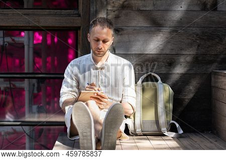 Stylish Young Man Author Writes Poem Uniting With Nature In Rays Of Sunlight. Focused Guy With Three