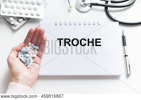 Troche Inscription On The Notebook Next To The Doctor's Hand With Tablets, Medical Concept