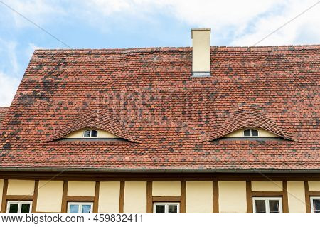 Old Beautiful European German Fachwerk Building Rooftop With Eye Shaped Windows And Chimney. Typical