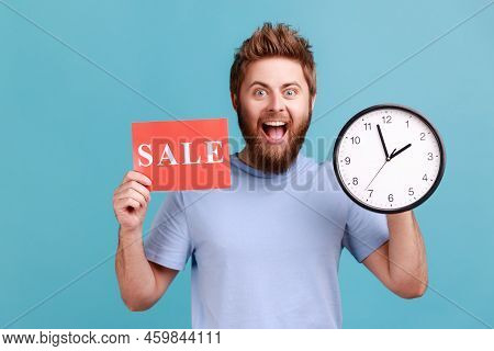 Portrait Of Excited Positive Handsome Bearded Man Holding Clock And Card With Sale Inscription, Anno