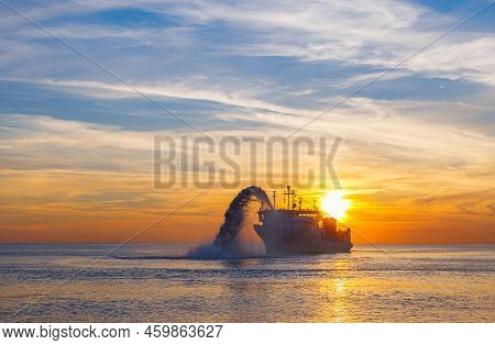 Vessel Engaged In Dredging At Sunset Time. Hopper Dredger Working At Sea. Ship Excavating Material F