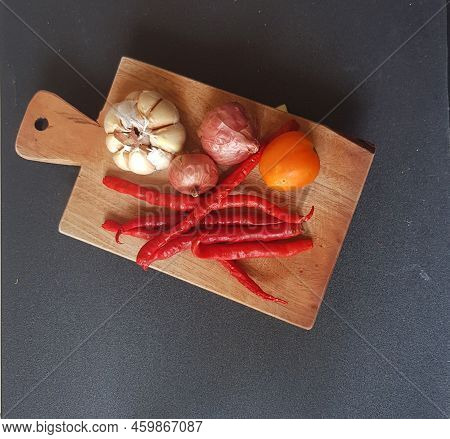 Garlic, Shallot, Chili And Tomato (samba L Ingredients) On A Wooden Board With A Black Background