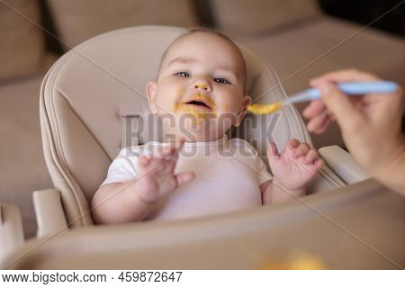 Mother Feeding Porridge To Her Happy Cheerful Baby Boy Using Spoon, Cheerful And Happy Baby Sitting 