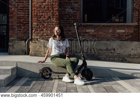 Young Woman In White Sneakers Is Sitting Near Electric Scooter