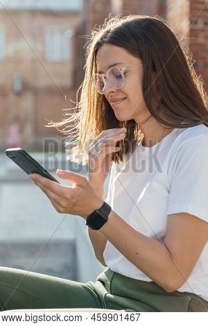 Young Female Sitting On Urban Stairs And Speaking On Smartphone