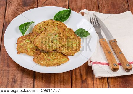 Fried Small Thick Savory Zucchini Pancakes On The White Dish, Cutlery On Napkin On The Old Rustic Ta