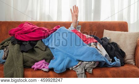 Dependence on things, conscious consumption of clothes, shopaholic, hand reaching out of a pile of c