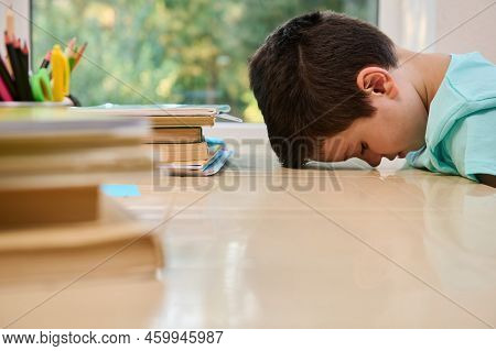 Tired Bored Schoolboy, Primary Student In Online School, Sitting At Desk, Leaning On The Table With 