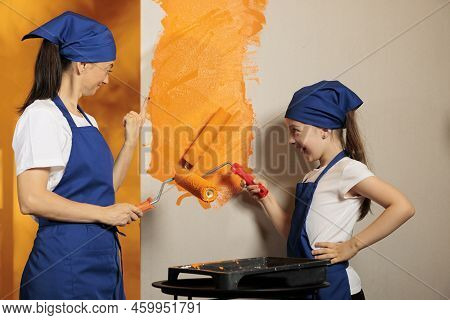 People Having Fun Painting Home Walls, Using Orange Paint Color To Redecorate Apartment Interior. Mo