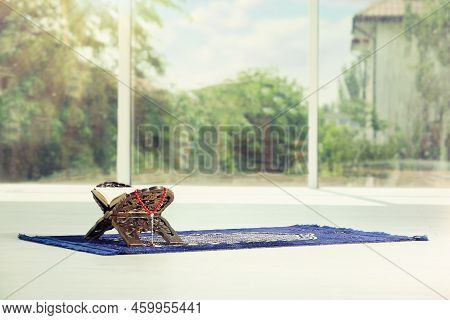 Rehal With Open Quran And Misbaha On Muslim Prayer Rug Near Window Indoors, Space For Text