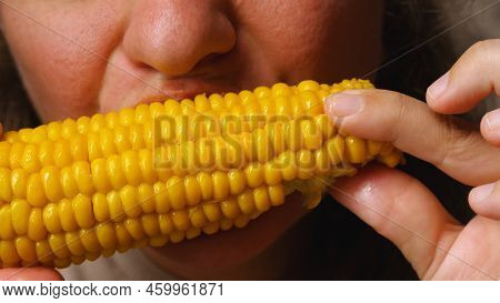 A Woman Eats Boiled Corn Sprinkled With Salt And Rubbed With Butter. Corn Cob In Hand. Close-up Fema