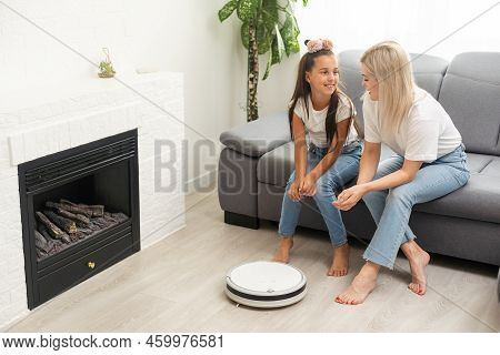 Cute Child Near Mother Looking At Robotic Vacuum Cleaner In Living Room