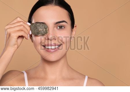 Beautiful Young Woman Putting Green Tea Bag On Eye Against Beige Background, Space For Text