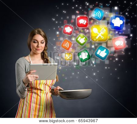 young woman cooking using the tablet, cloud of colorful social media icons out of tablet pc