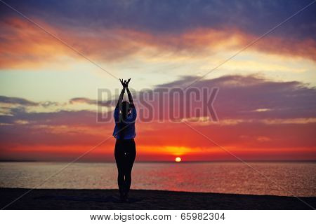 Fine silhouette of a slender woman doing yoga on the sea with sunrise