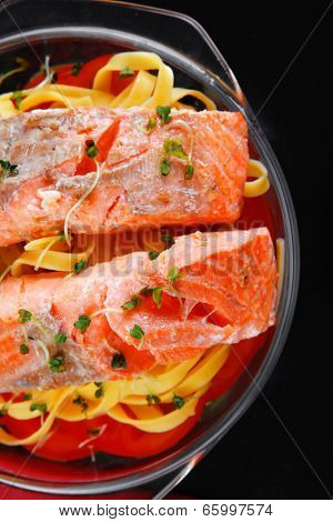 fresh fried natural pink salmon on italian traditional tagliatelle backed with tomato and vegetables served over black wooden table