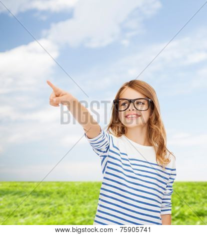 education, school and imaginary screen concept - cute little girl in eyeglasses pointing in the air or imaginary screen