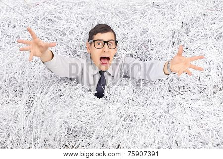 Terrified young man drowning in a pile of shredded paper 