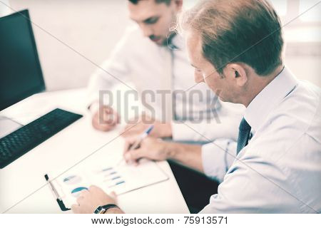 businesss and office concept - businessmen with notebook discussing graphs on meeting