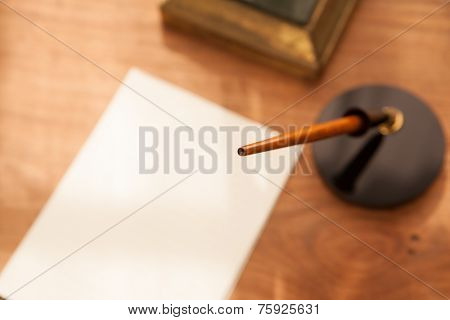 Retro style pen, pen stand and paper or memo on wooden desk. Focus is on pen tip. 