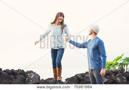 Happy Young Couple Having Fun Outdoors. Man helping attractive girlfriend over rock wall. Chivalry Concept, Romantic Date.