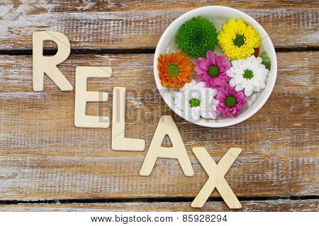 Relax written with wooden letters on rustic surface with Santini flowers